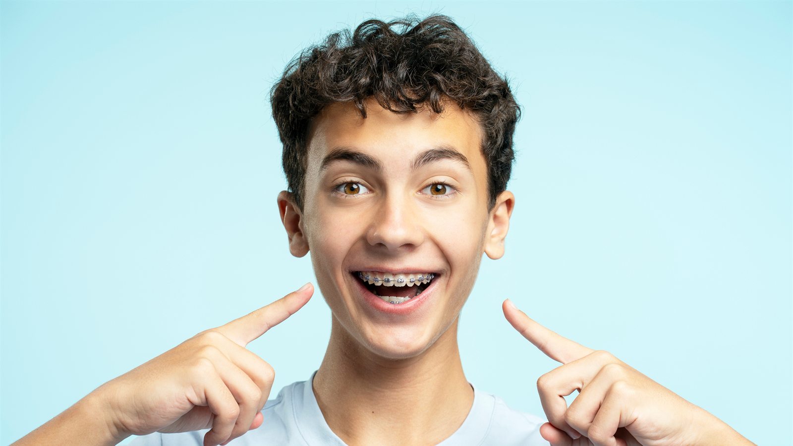 Smiling boy wearing braces pointing at his teeth